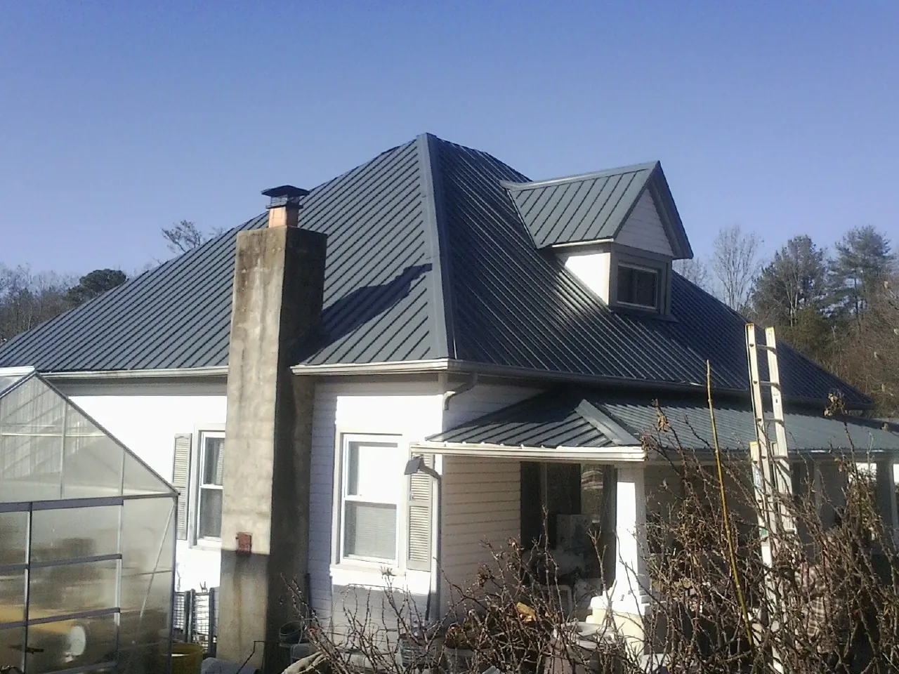 Dark blue standing seam metal roof on a white farmhouse with dormer — Slate & Tile Roof Repair by Roofing Brothers in Walkertown