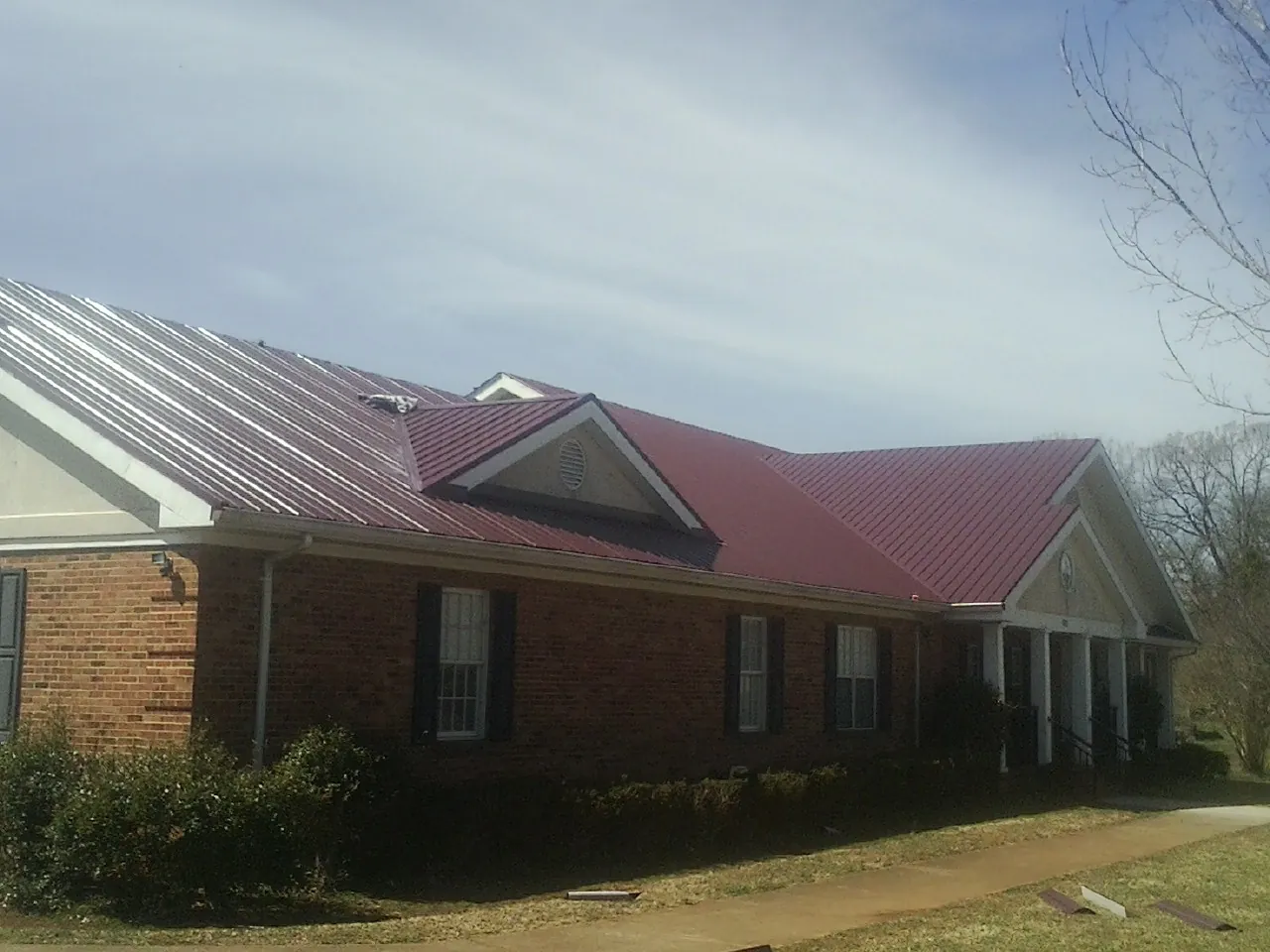 Red metal roof with gabled entries on a long brick building, from a Hail Damage Roof Repair job in Walkertown