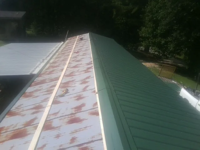 Old rusted panels beside newly installed green metal roofing — Wind Damage Roof Repair by Roofing Brothers in Walkertown