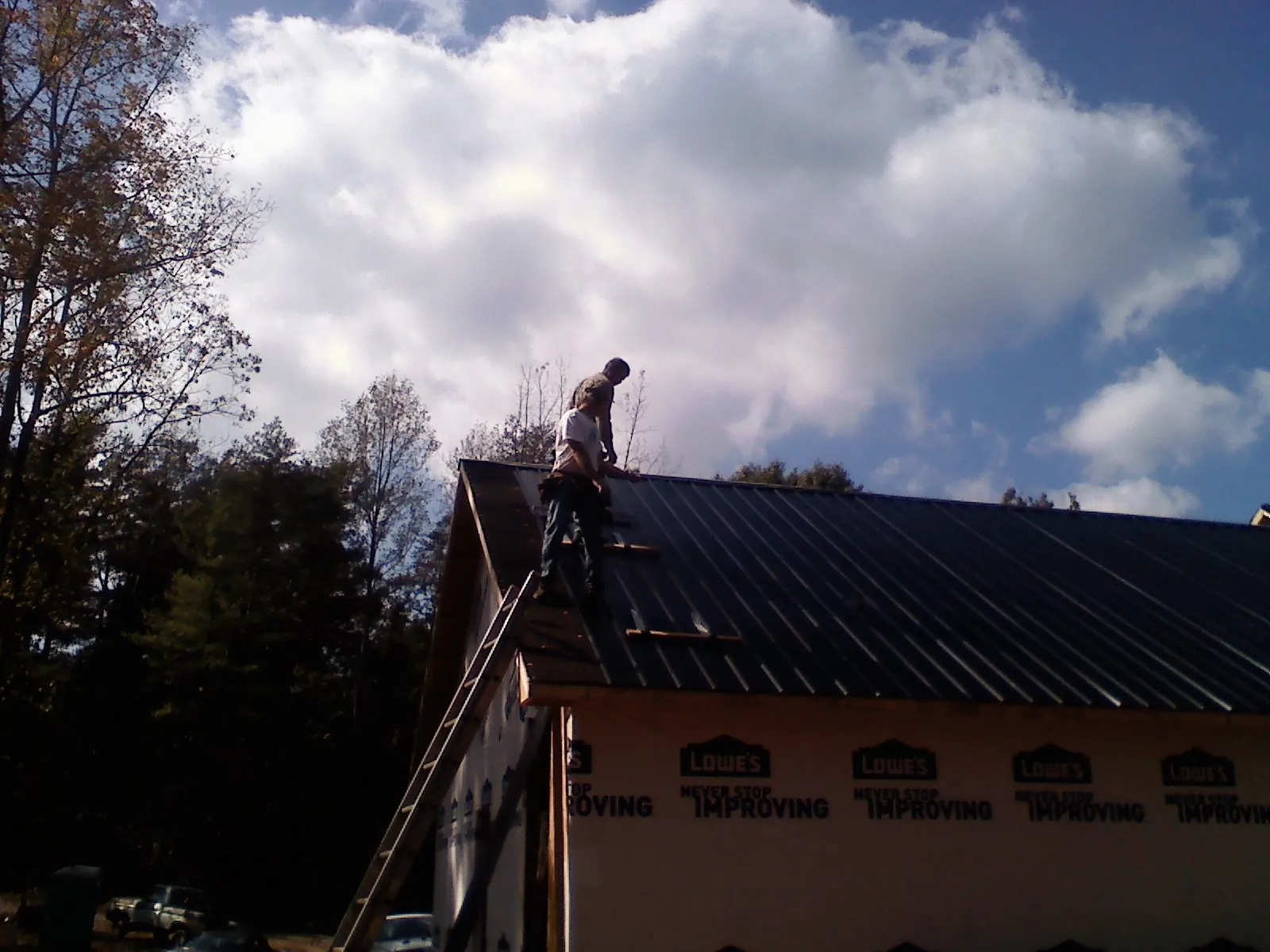 Roofer fastening dark metal panels high against a cloudy sky in Walkertown