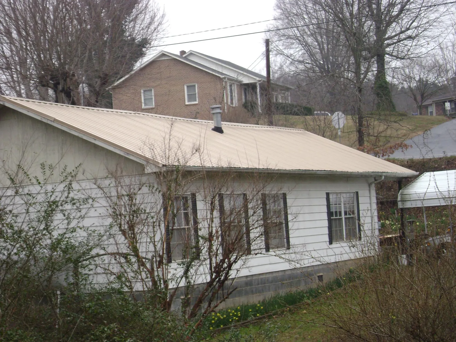 Tan metal roof on a white sided house set into a hillside — Commercial Roofing by Roofing Brothers in Walkertown